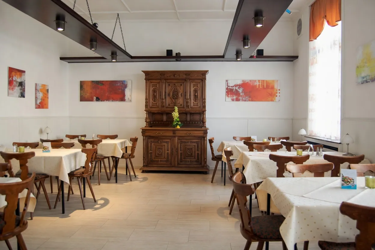 Heller Saal mit geschnitztem Eichenschrank, moderner Kunst an den Wänden und eingedeckten Tischen